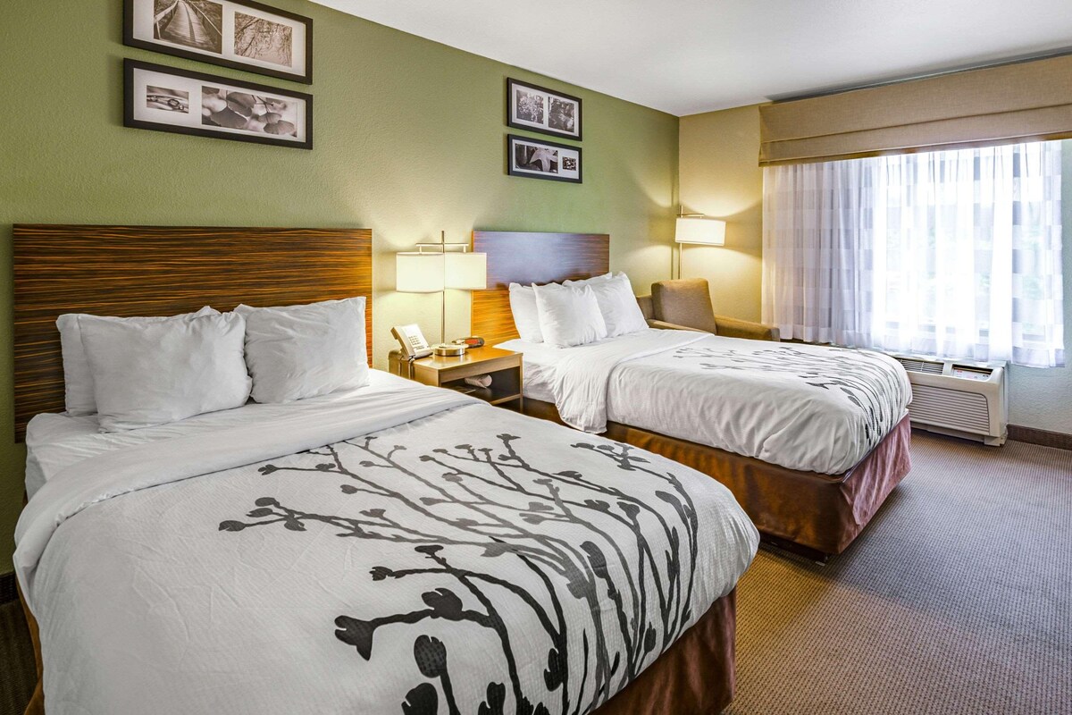 A hotel room with two beds, a nightstand with a lamp, and a window with curtains.