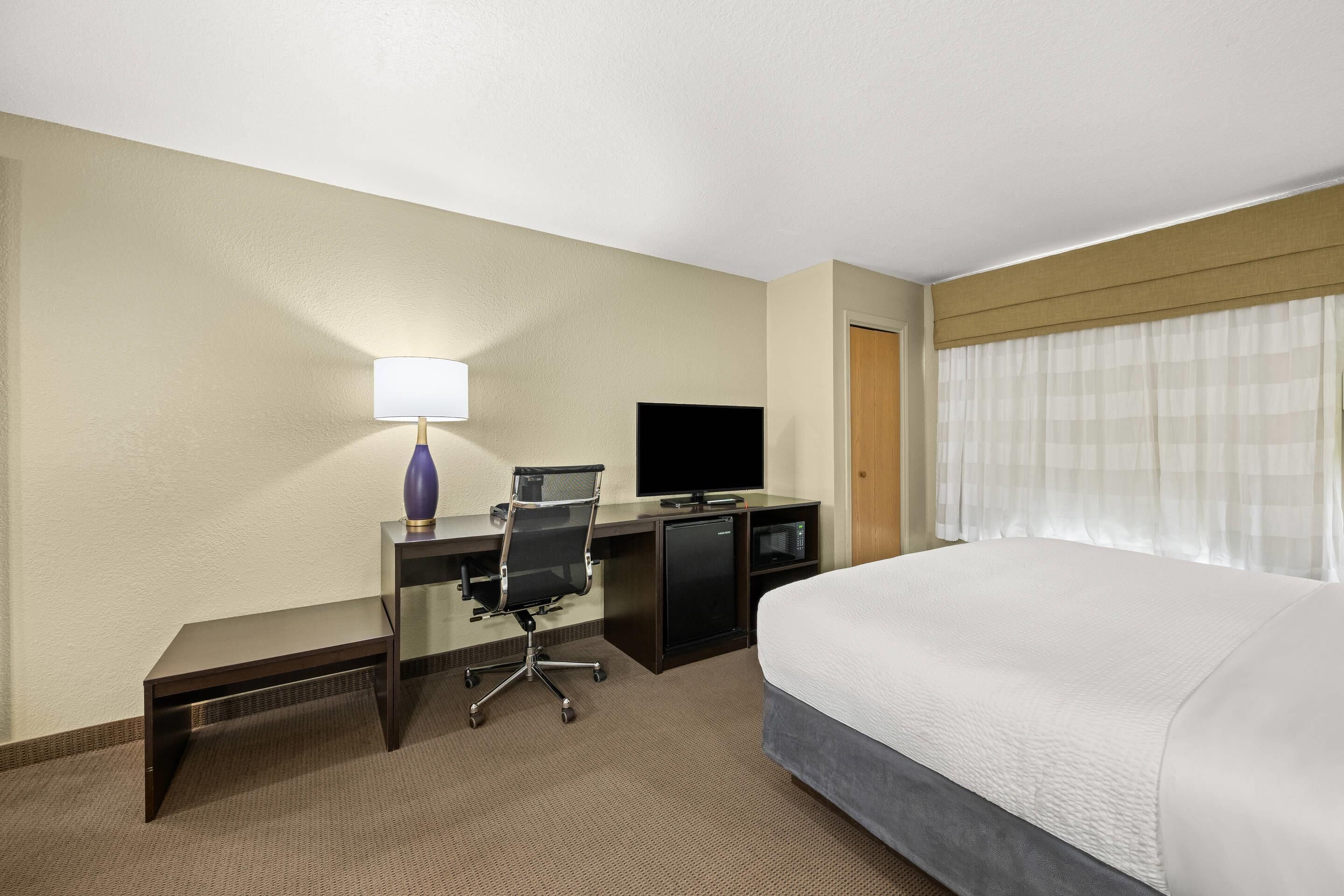 A hotel room with a bed, desk, chair, TV, and a lamp.