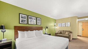 A hotel room with a large bed, a nightstand, a lamp, a sofa, and framed pictures on the wall. - Sleep Inn Boone University Area (Boone)