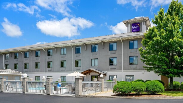 A multi-story hotel with a modern design, featuring a swimming pool area with lounge chairs and umbrellas, and a well-maintained garden with trimmed bushes.