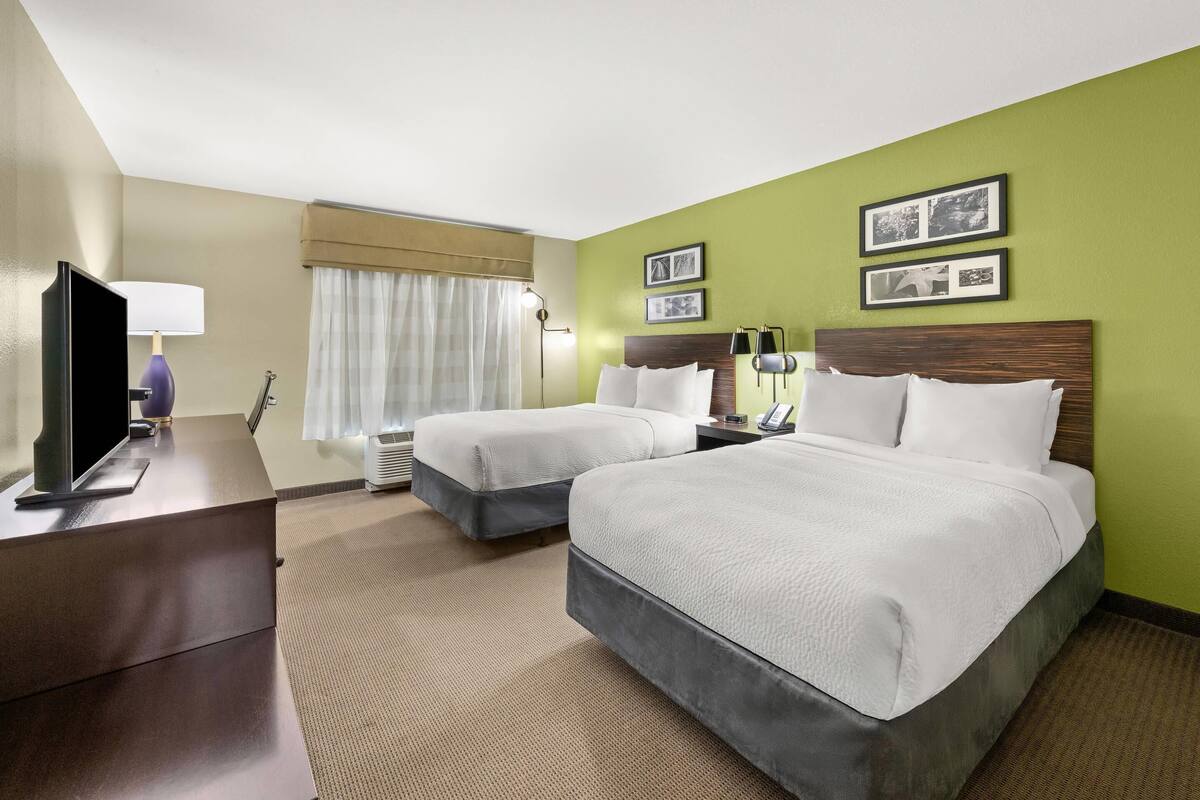 A hotel room with two beds, a desk with a TV, a lamp, and a window with curtains.