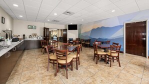 A dining area with multiple tables and chairs, a kitchen area with a counter and appliances, and a mural on the wall depicting a mountain landscape.