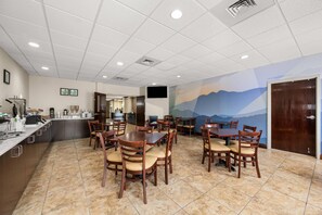 A dining area with multiple tables and chairs, a kitchen area with a counter and appliances, and a mural on the wall depicting a mountain landscape. - Sleep Inn Boone University Area (Boone)