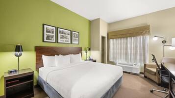 Habitación de hotel con una cama grande, un escritorio, una silla, una mesita de noche con lámpara y un teléfono en la pared.