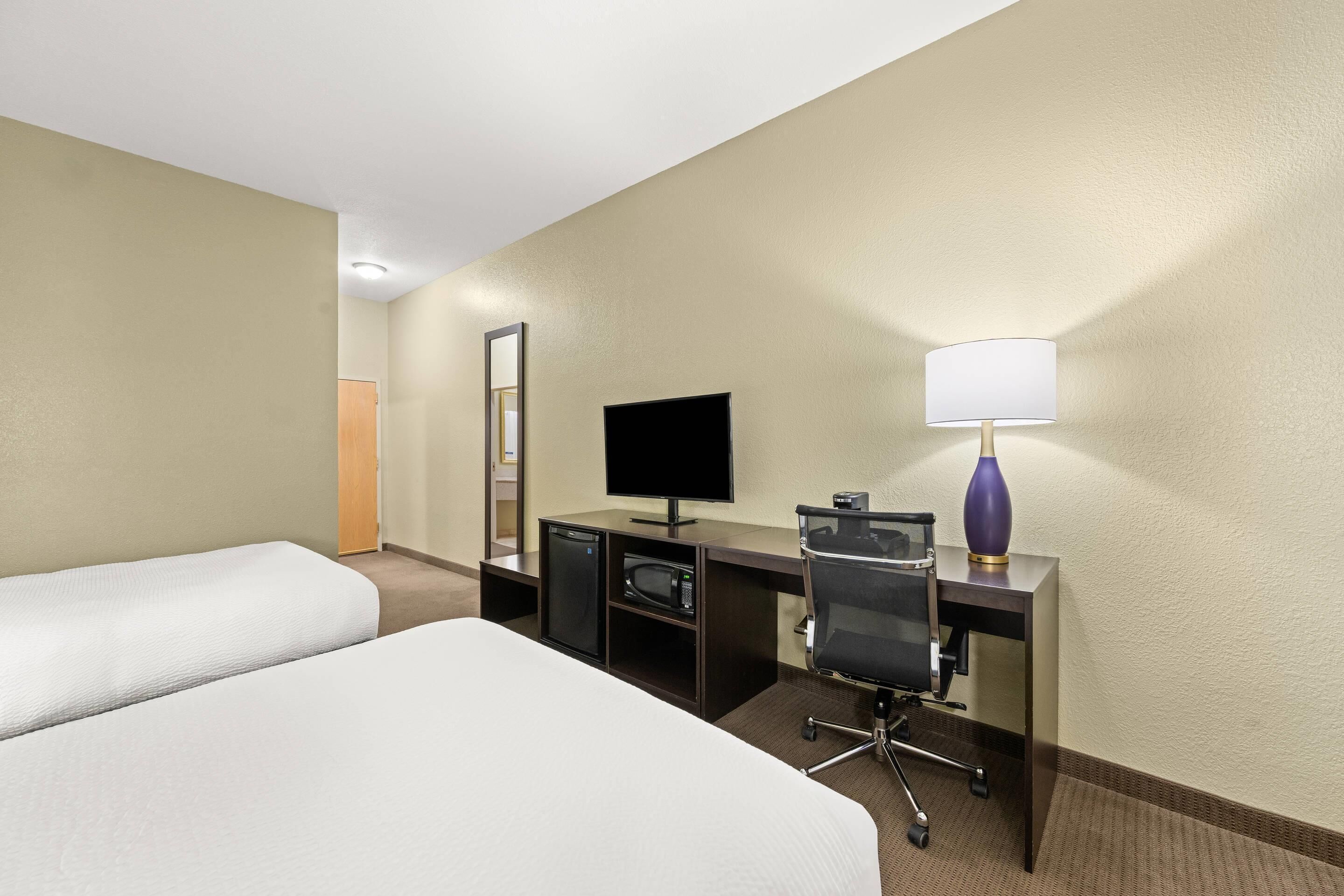 A hotel room with two beds, a desk with a computer, a television, and a lamp.