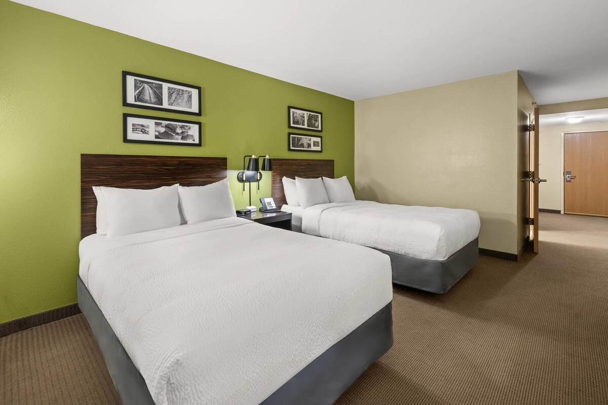 A hotel room with two beds, a nightstand with a lamp, and two framed pictures on the wall.