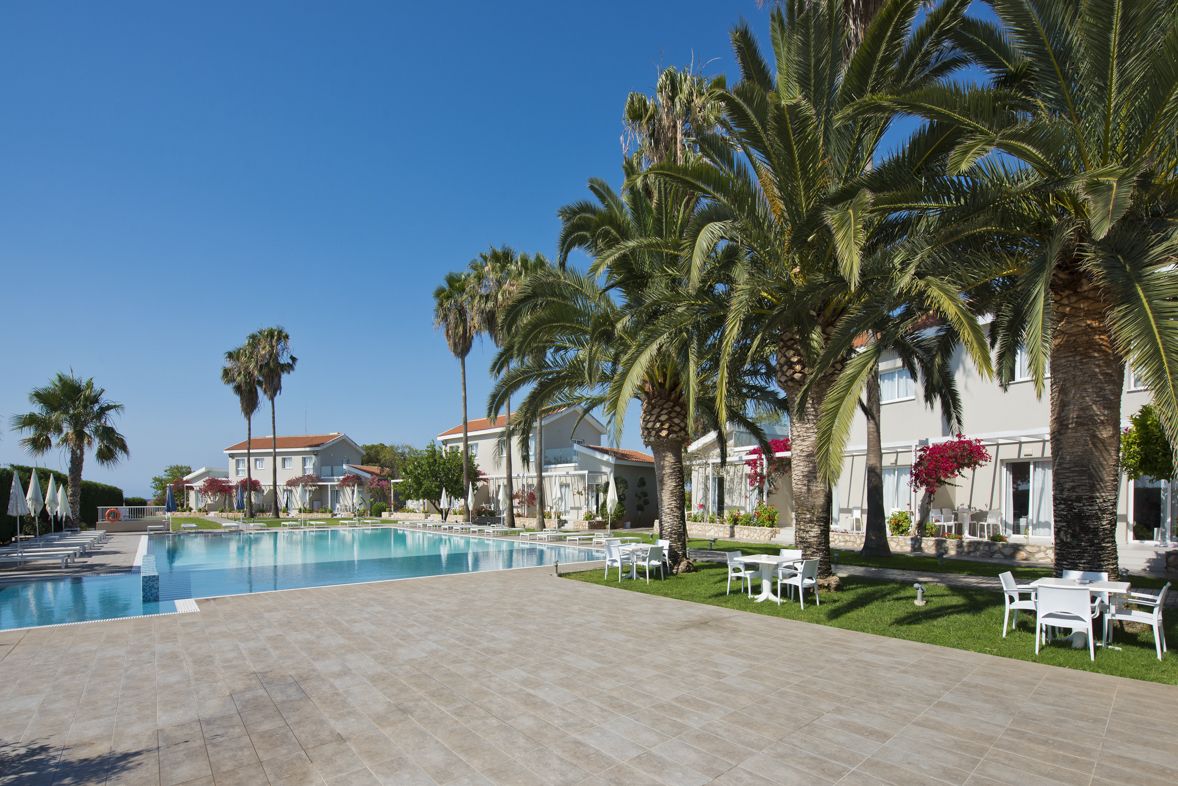 A pool area with palm trees, outdoor seating, and buildings in the background.