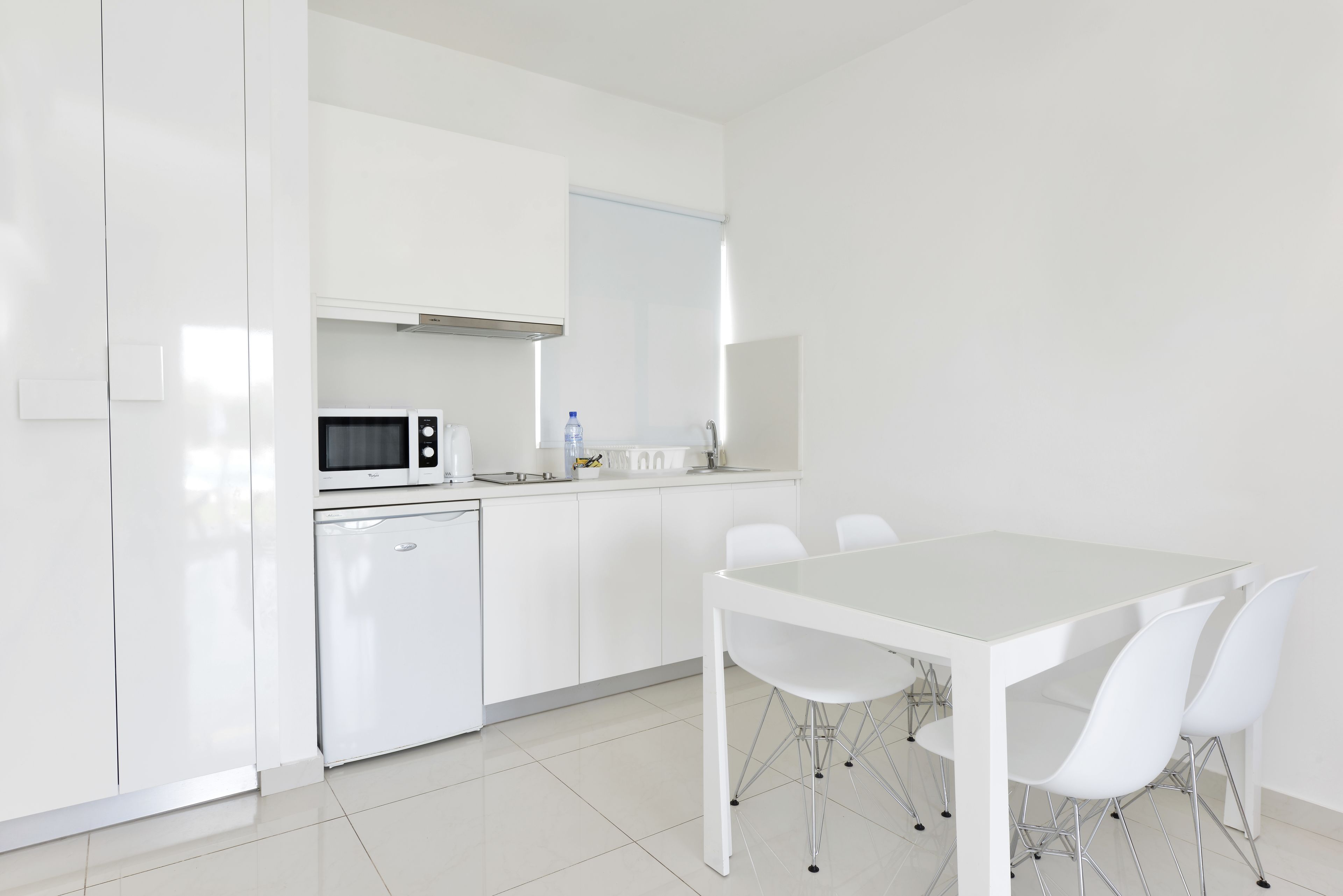 A modern kitchen with white cabinets, a microwave, a small refrigerator, and a dining table with four chairs.