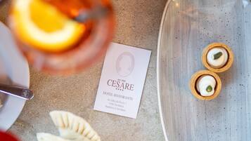 A table with a dessert plate containing two small pastries, a card with hotel information, and a glass of a beverage.