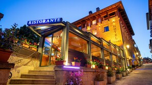 A hotel with a restaurant on the ground floor, featuring a glass entrance and outdoor seating with potted plants. - Hotel Cesare (San Marino)
