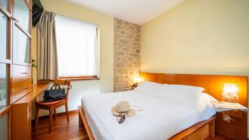 Un dormitorio ordenado con cama, una silla, un escritorio y una mesita de noche.