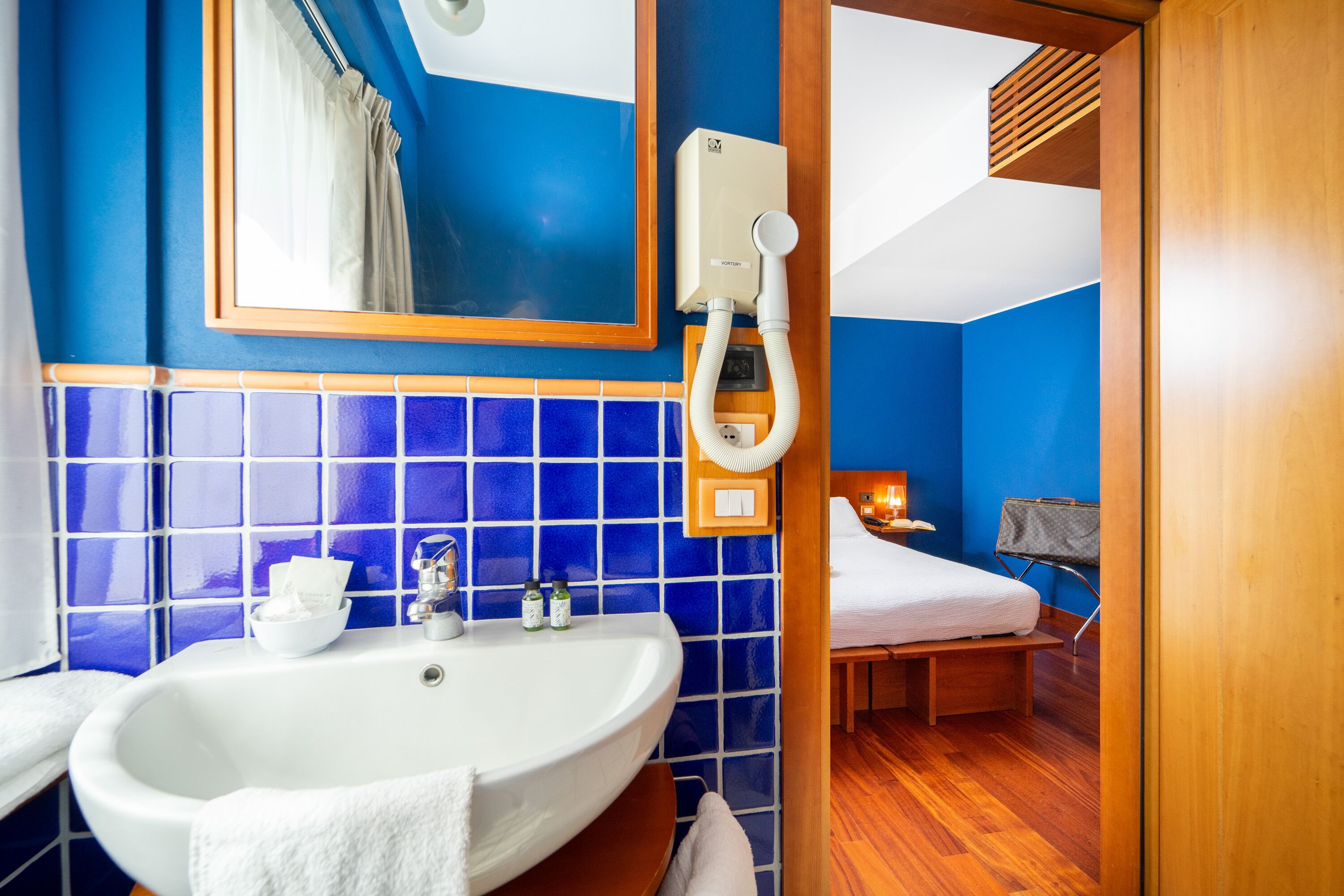 Un baño con lavamanos blanco, paredes con azulejos azules, un espejo y una cortina de ducha.