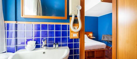 Un baño con lavamanos blanco, paredes con azulejos azules, un espejo y una cortina de ducha.