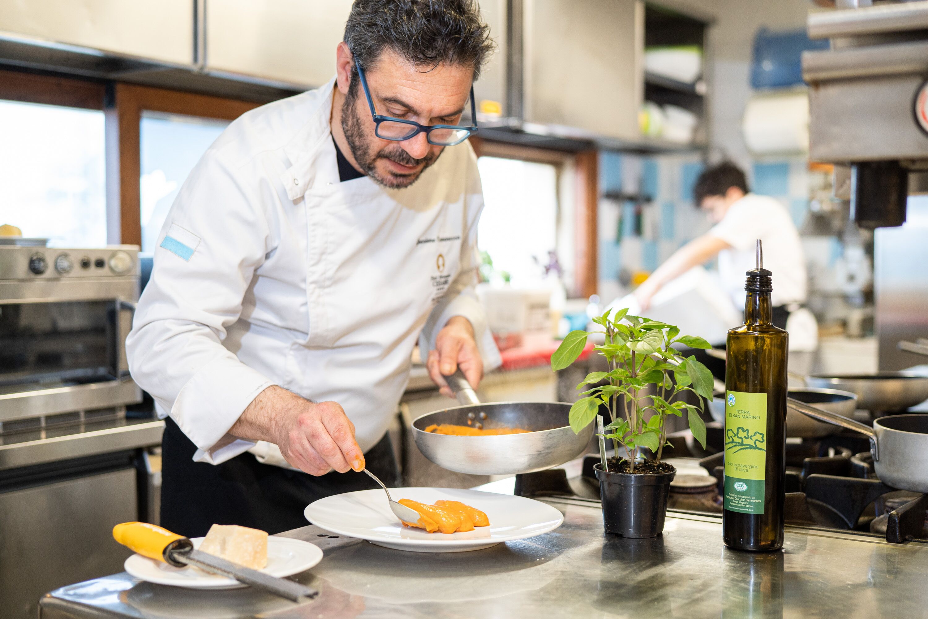Un chef préparant des plats dans une cuisine professionnelle équipée d’appareils en acier inoxydable et agrémentée d’une plante en pot.