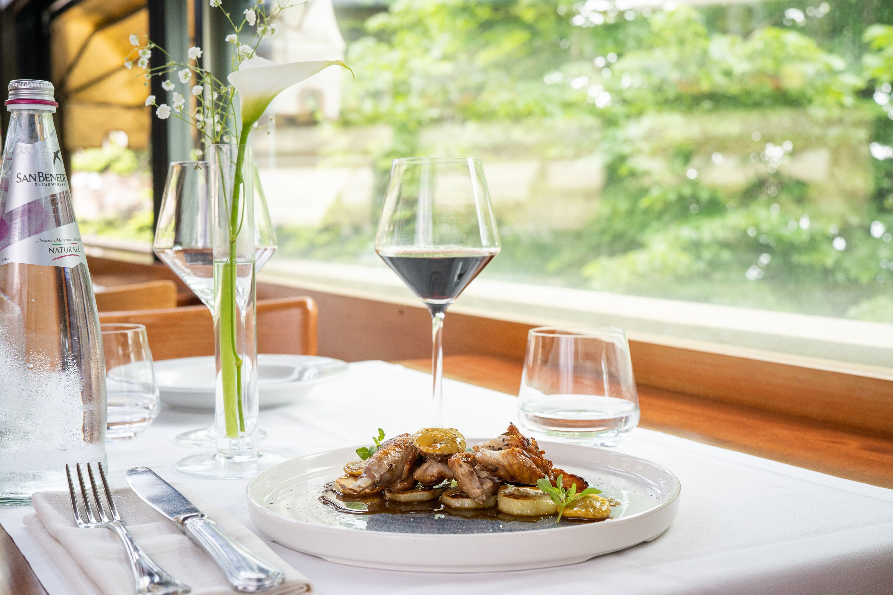 A dining table with a plate of food, a bottle of water, and wine glasses.