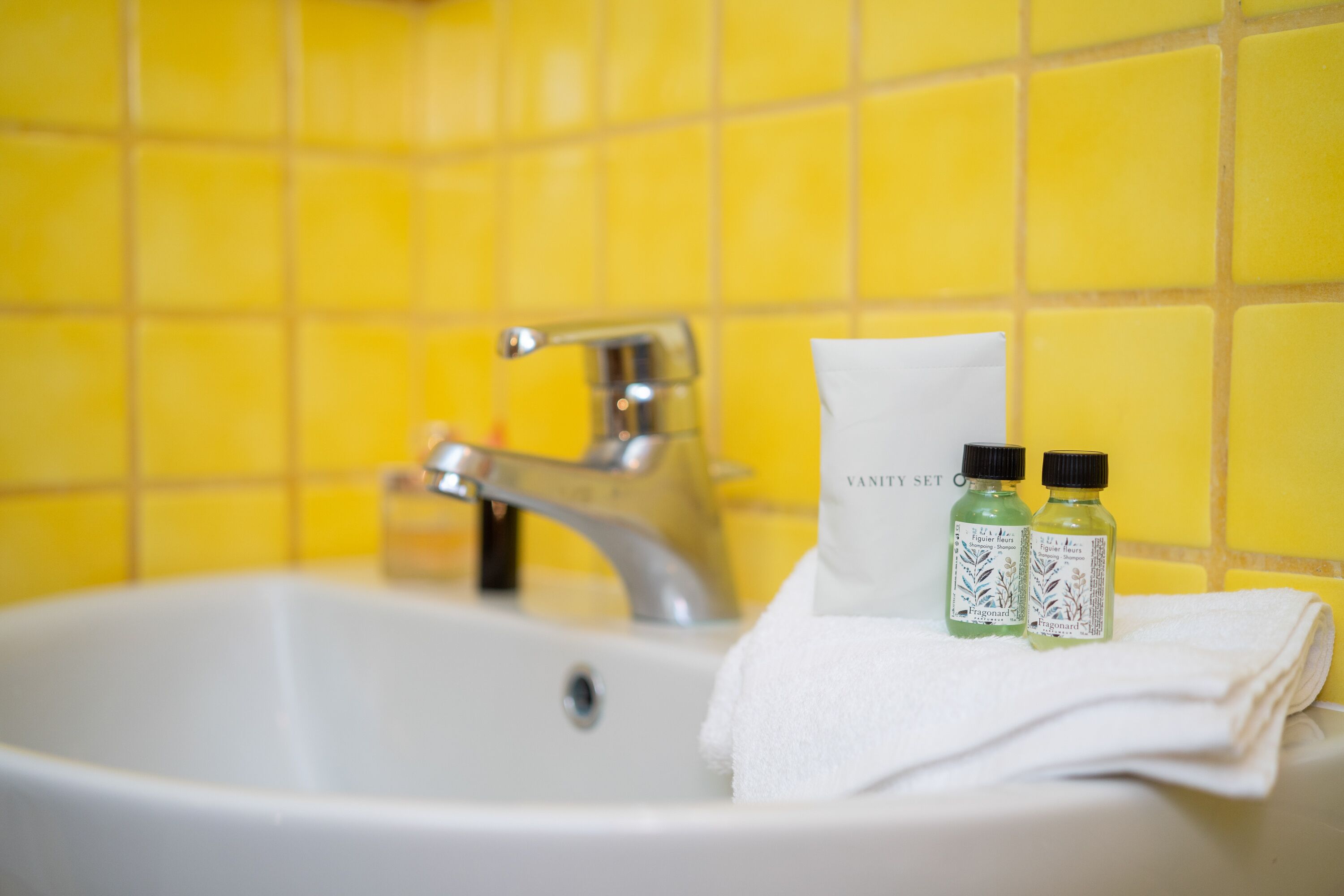 A bathroom sink with yellow tiles, a white towel, and two bottles of toiletries.