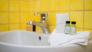 A bathroom sink with yellow tiles, a white towel, and two bottles of toiletries.