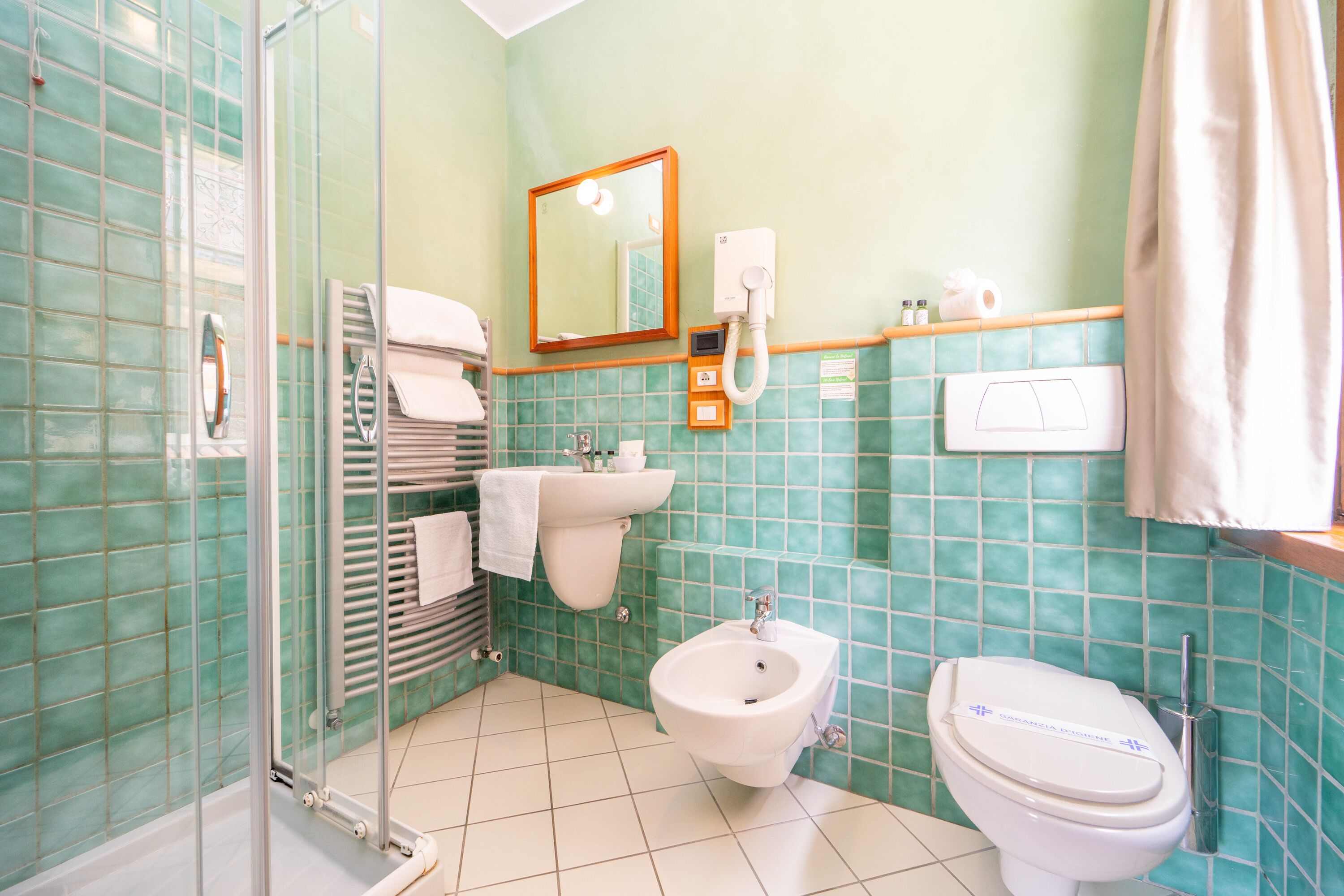 Une salle de bain dotée d’une douche à parois de verre, d’un bidet, de toilettes, d’un lavabo et d’un miroir.