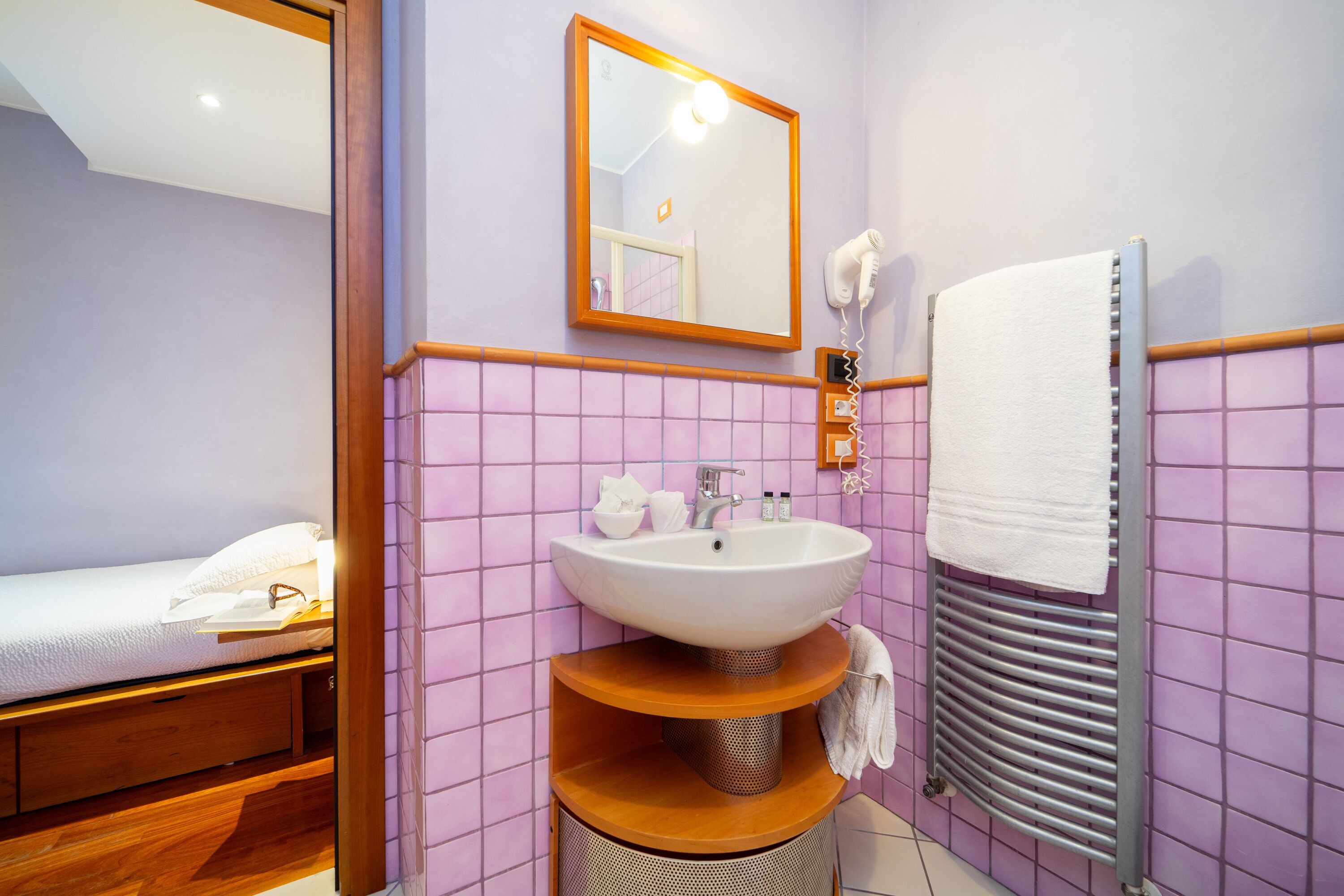 Un baño con cama, lavamanos, espejo y toallero.