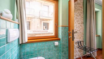 Un baño con inodoro, una ventana con cortinas, dispensador de toallas y un tendedero.