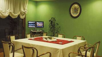 A conference room with a green wall, a table with a red placemat, and two monitors on a stand.