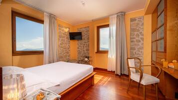 A hotel room with a large bed, a wooden desk, a chair, a television, and a view of the mountains.