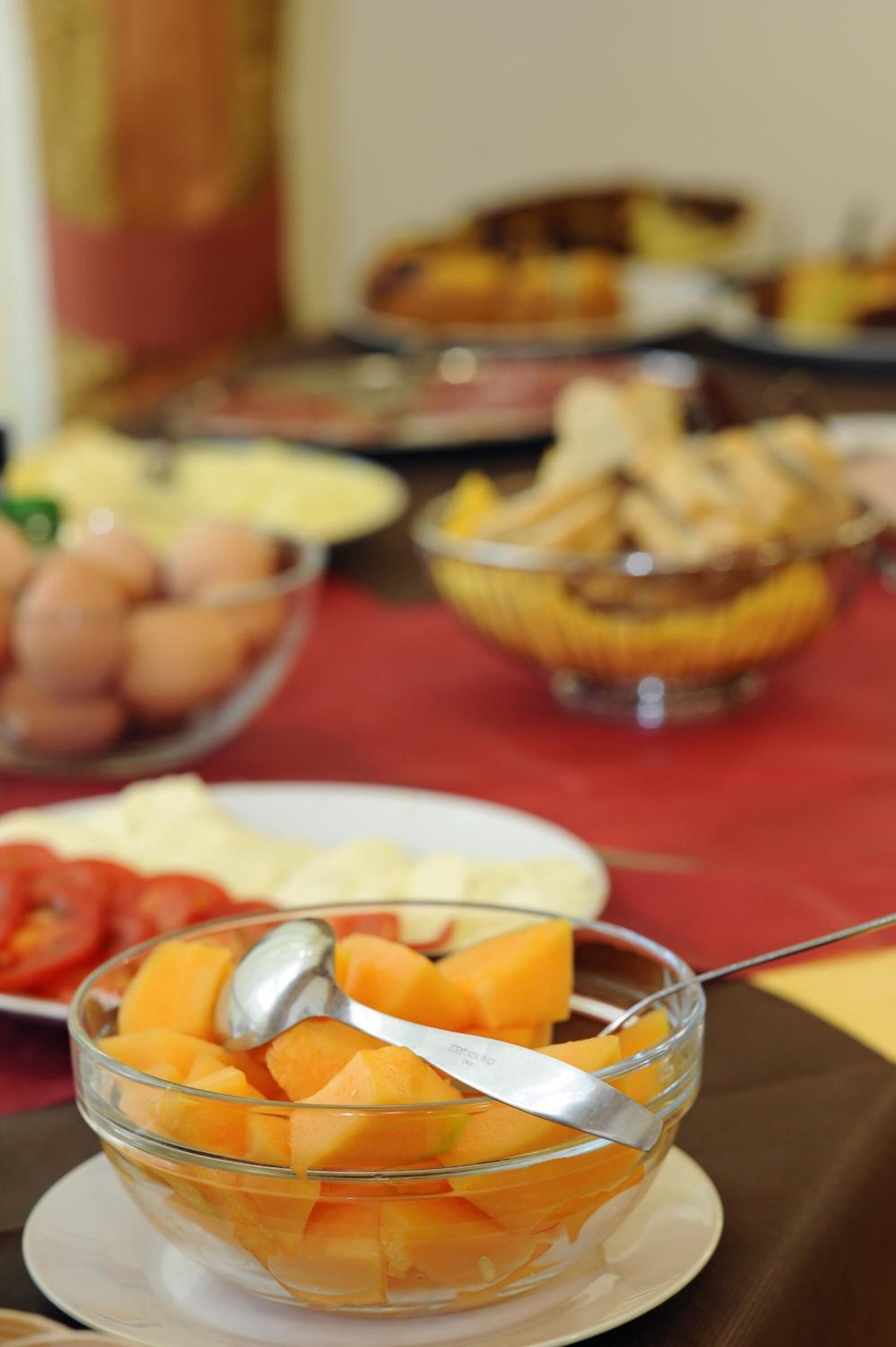 Ein Tisch mit verschiedenen Speisen, darunter eine Schüssel mit gewürfeltem Obst, möglicherweise Melonenkugeln, und weitere Gerichte im Hintergrund.