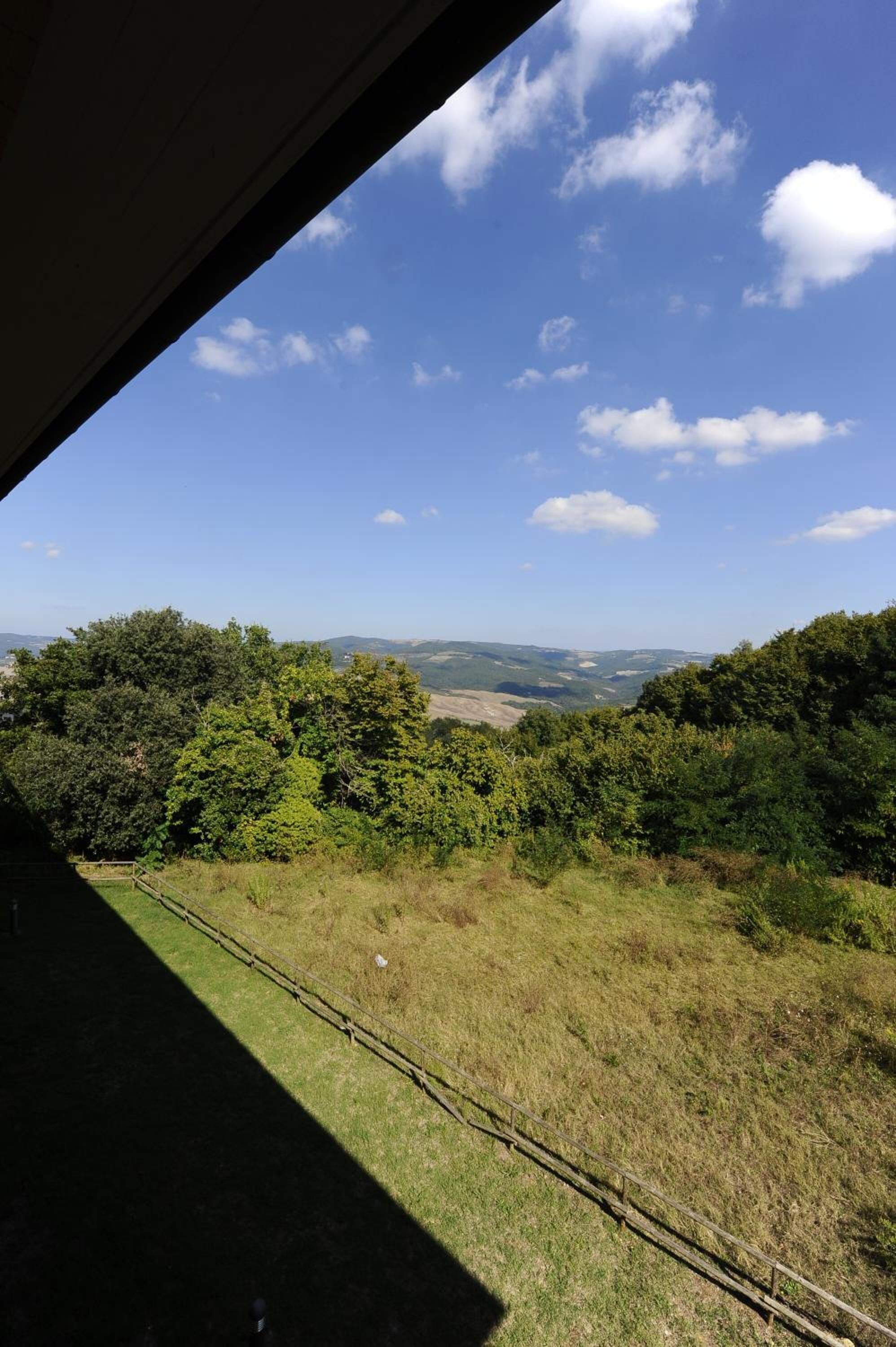 A view from inside a building looking out at a grassy landscape with trees and a clear sky.