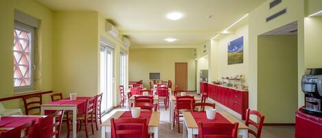 A dining area with red tables and chairs, a kitchen area with red cabinets, and a television in the background.