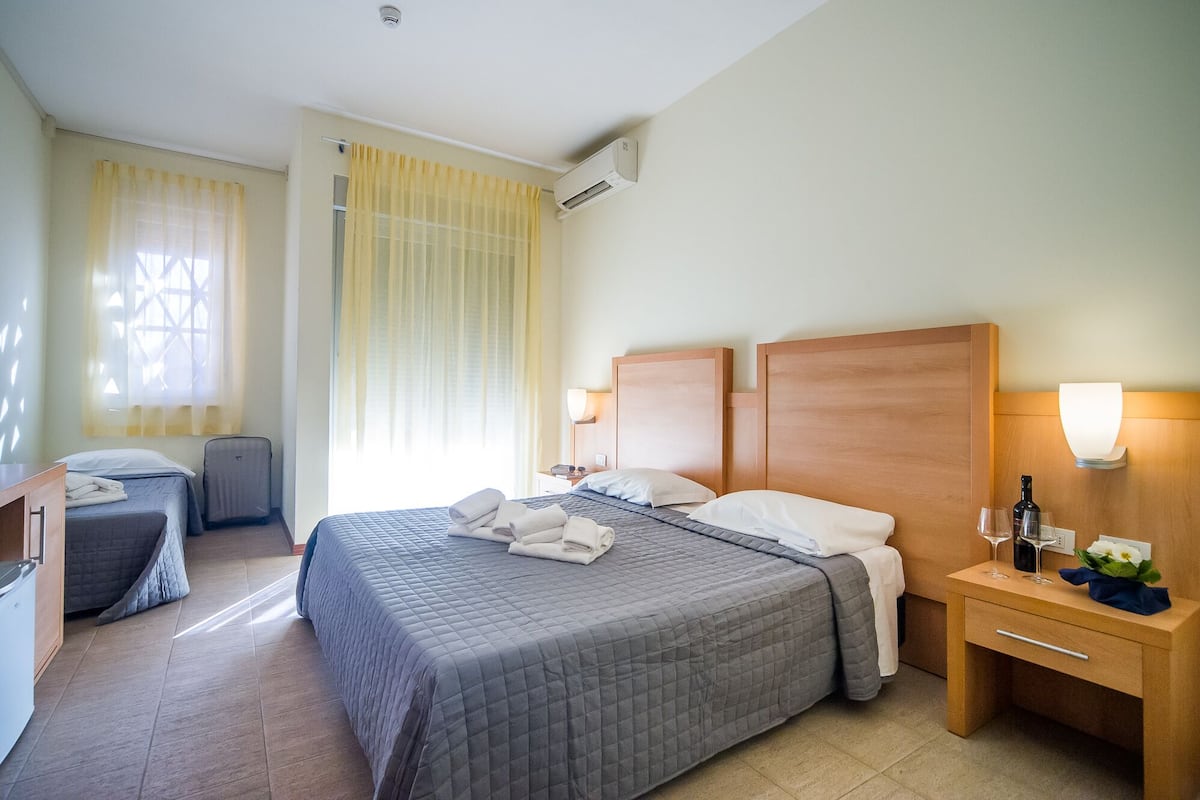 A hotel room with a large bed, a bedside table with a lamp, a small desk, and a chair.