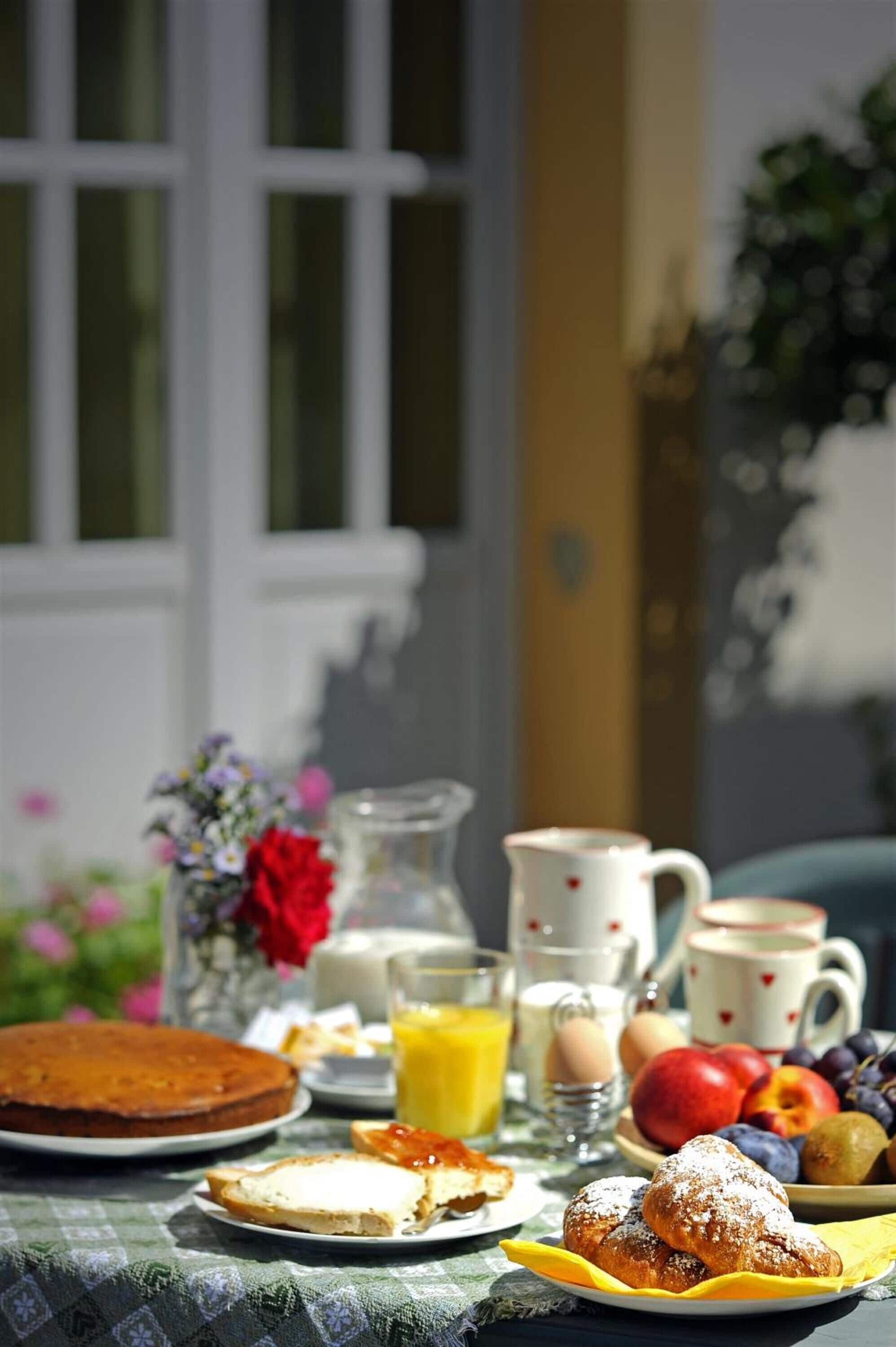 Una mesa de desayuno con pastel, bollería, fruta y bebidas.