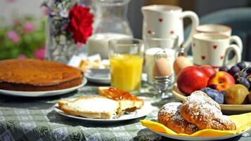 Una mesa de desayuno con pastel, bollería, fruta y bebidas.