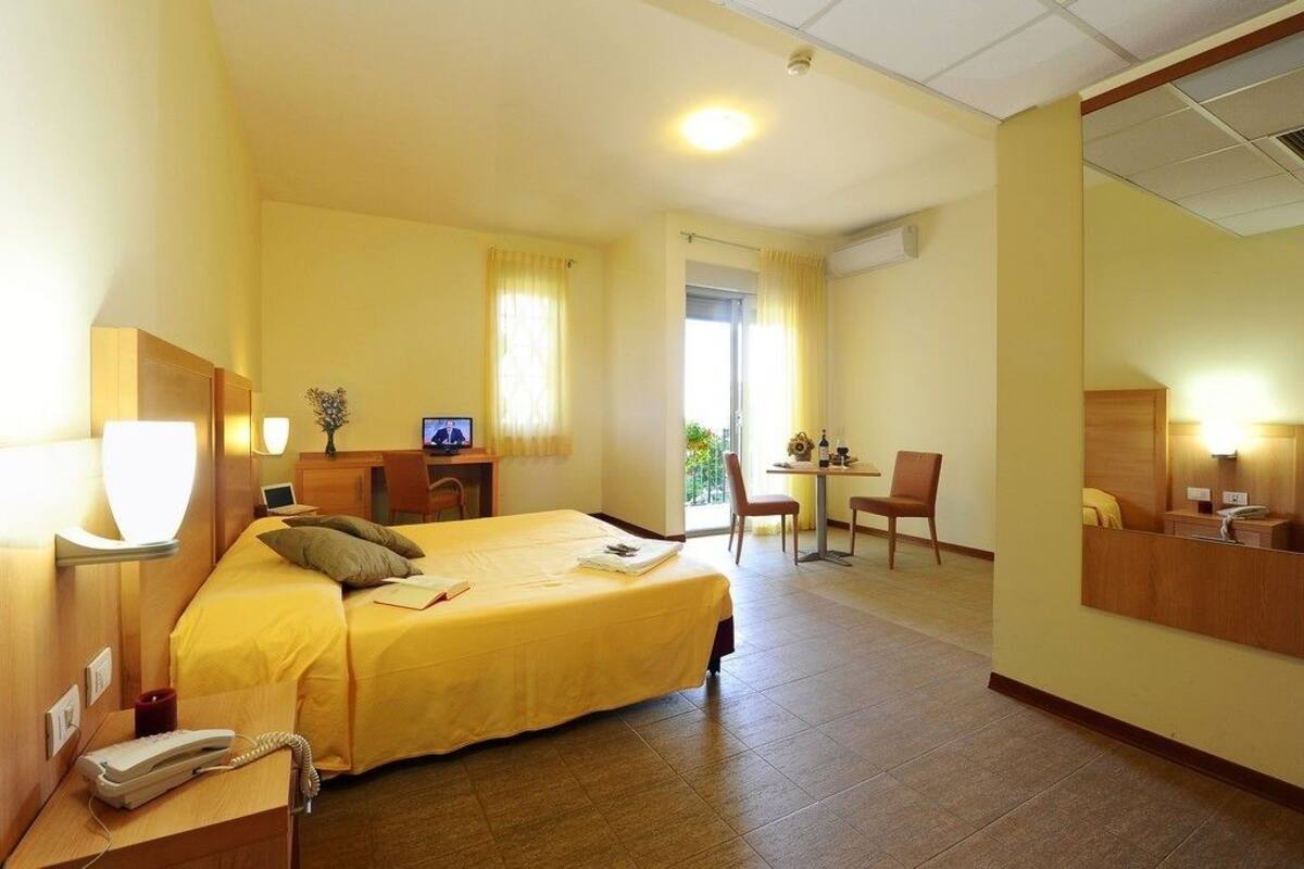 A hotel room with a bed, desk, chair, and a mirror.