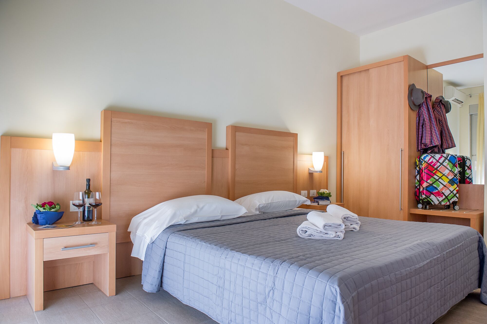 A hotel room with a large bed, wooden headboard, bedside tables with lamps, a mirror, and a wardrobe.