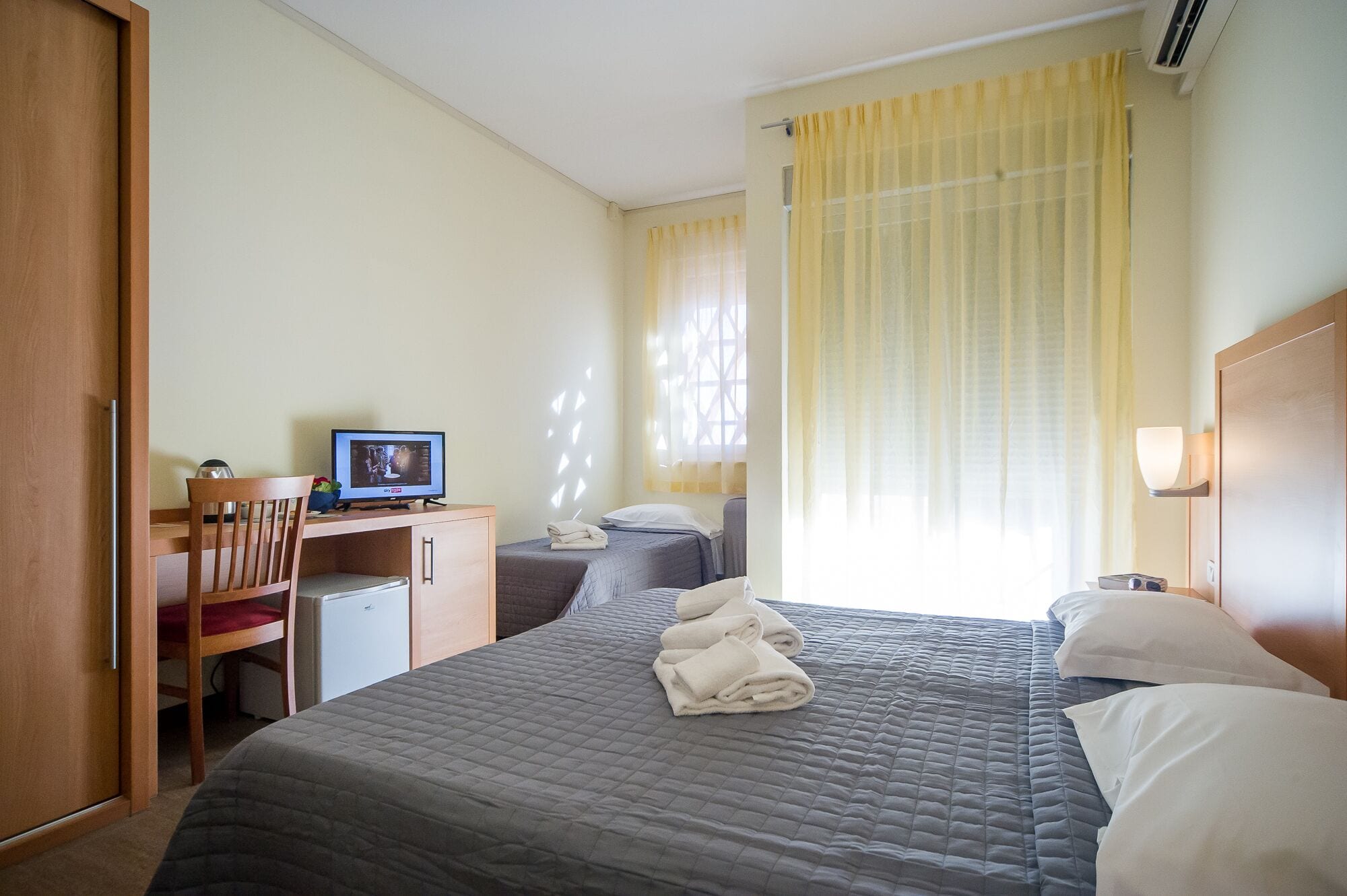 Una habitación de hotel con cama, escritorio con computadora, silla y una kitchenette pequeña.