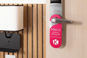 Un picaporte con una tarjeta roja que dice “Merci de ne pas déranger” y un logotipo.