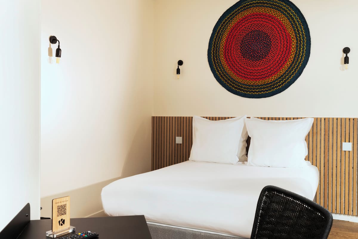 Ein Hotelzimmer mit einem Bett, einem Schreibtisch mit einem Laptop, einem Stuhl, einer Wandleuchte und einem Wandbild.