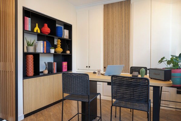 A modern kitchen with a wooden cabinet, a black bookshelf, two wicker chairs, a laptop, and a Marshall radio.