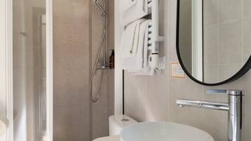 Een moderne badkamer met een douchecabine van glas, een wit toilet, een rond wastafel met een chromen kraan en een handdoekrek met opgevouwen handdoeken.