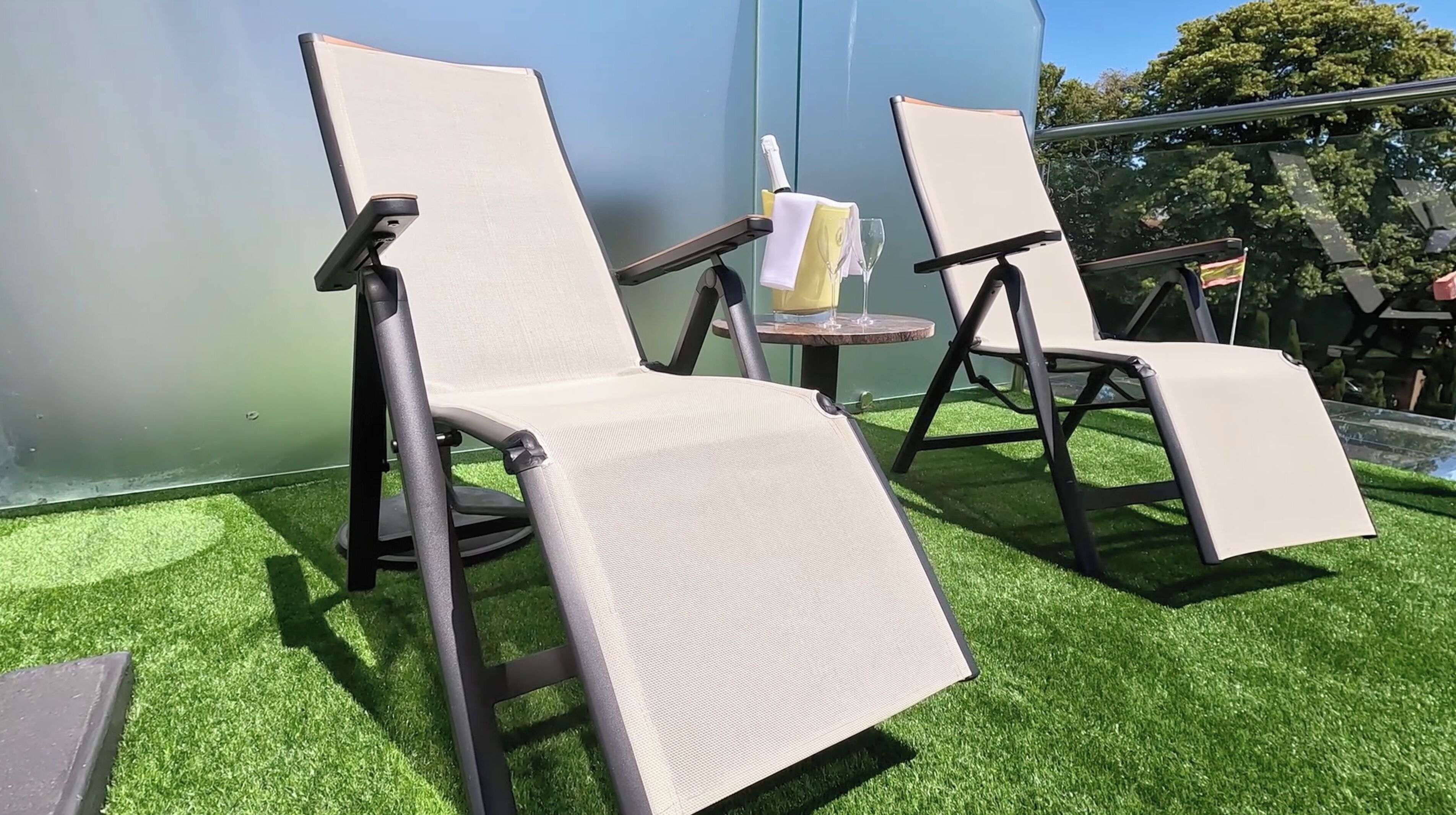 Two lounge chairs with a table and a bottle of champagne on a green artificial grass surface.