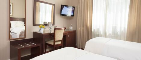 Habitación de hotel con cama, escritorio con silla, televisor y ventana con cortinas.