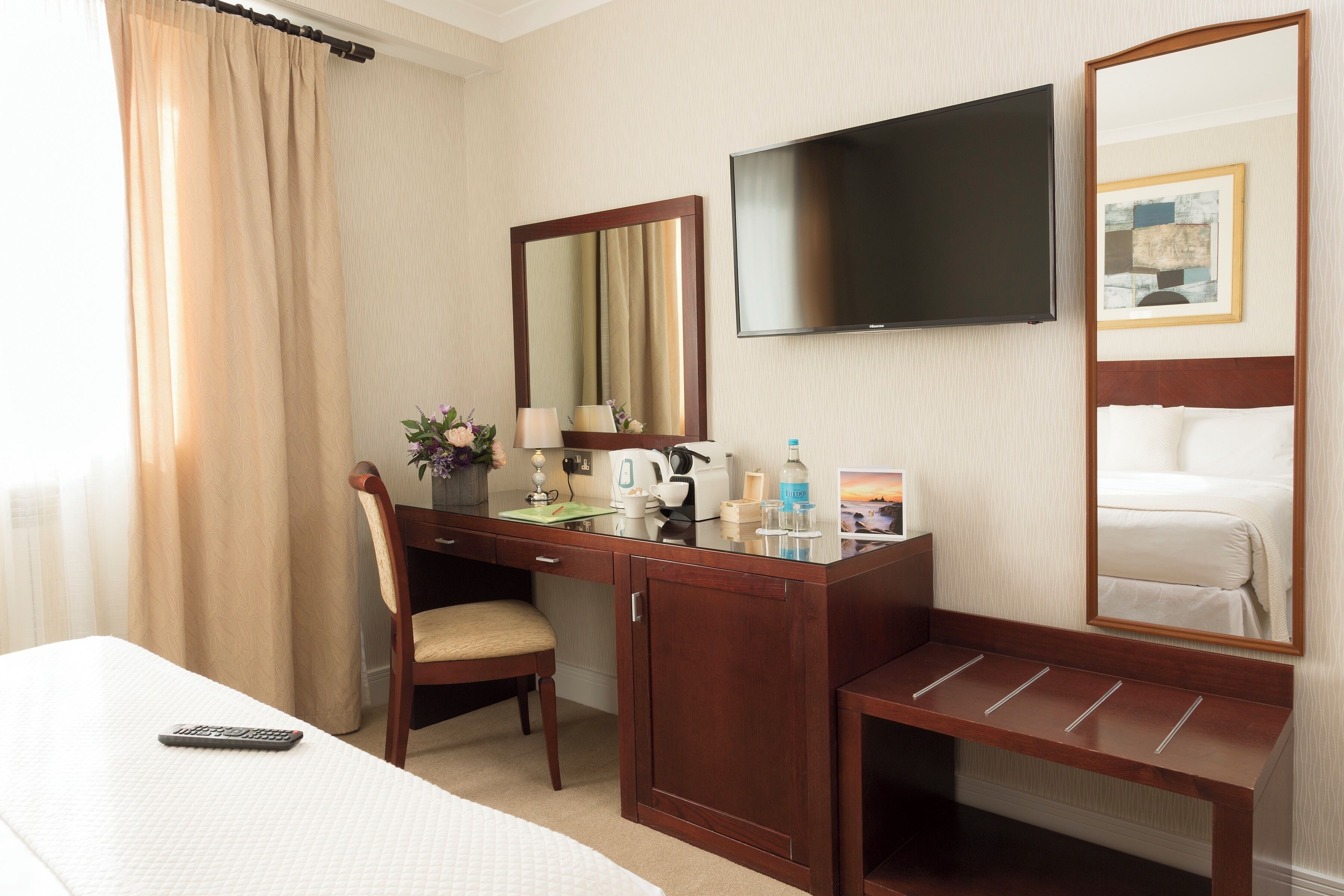 A hotel room with a bed, a desk with a chair, a TV, and a mirror.