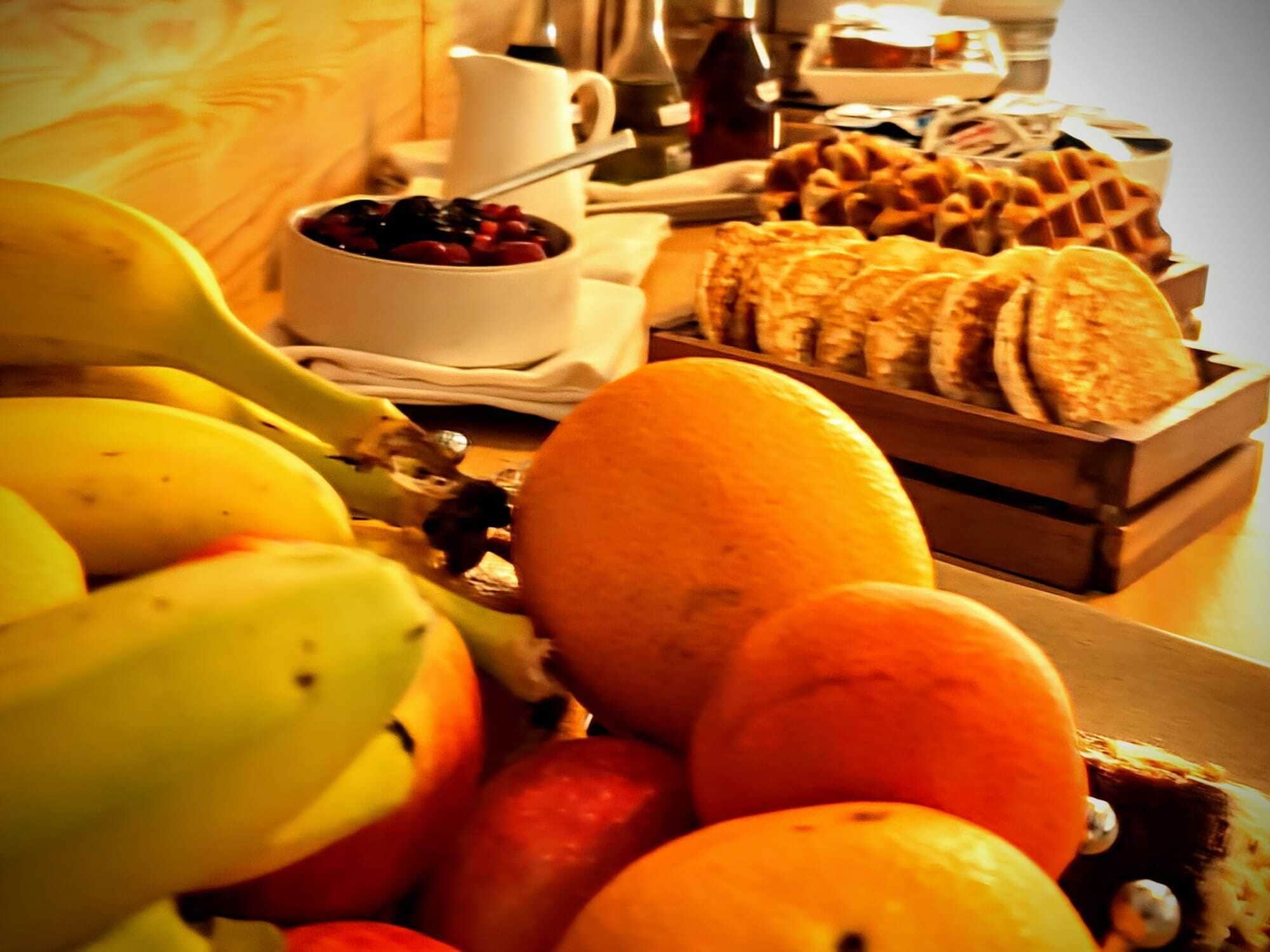 Una mesa de desayuno con frutas, gofres y una taza de café.