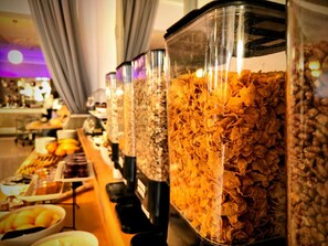 A buffet line with various food items, including a large container of cereal and bowls of fruit. - The Savoy Jersey (St. Helier)