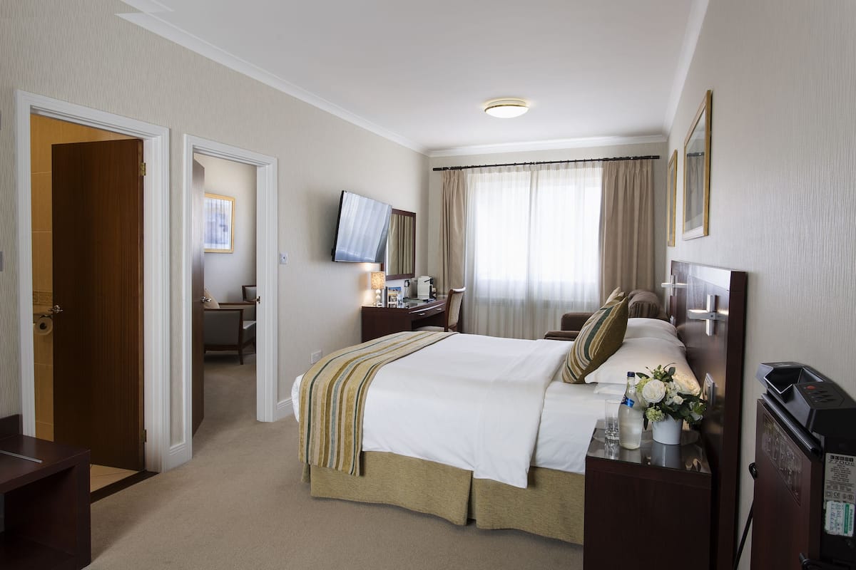 Ein Hotelzimmer mit Bett, Nachttisch, Fernseher, Schreibtisch und Vorhängen.