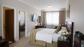 A hotel room with a bed, bedside table, TV, desk, and curtains.