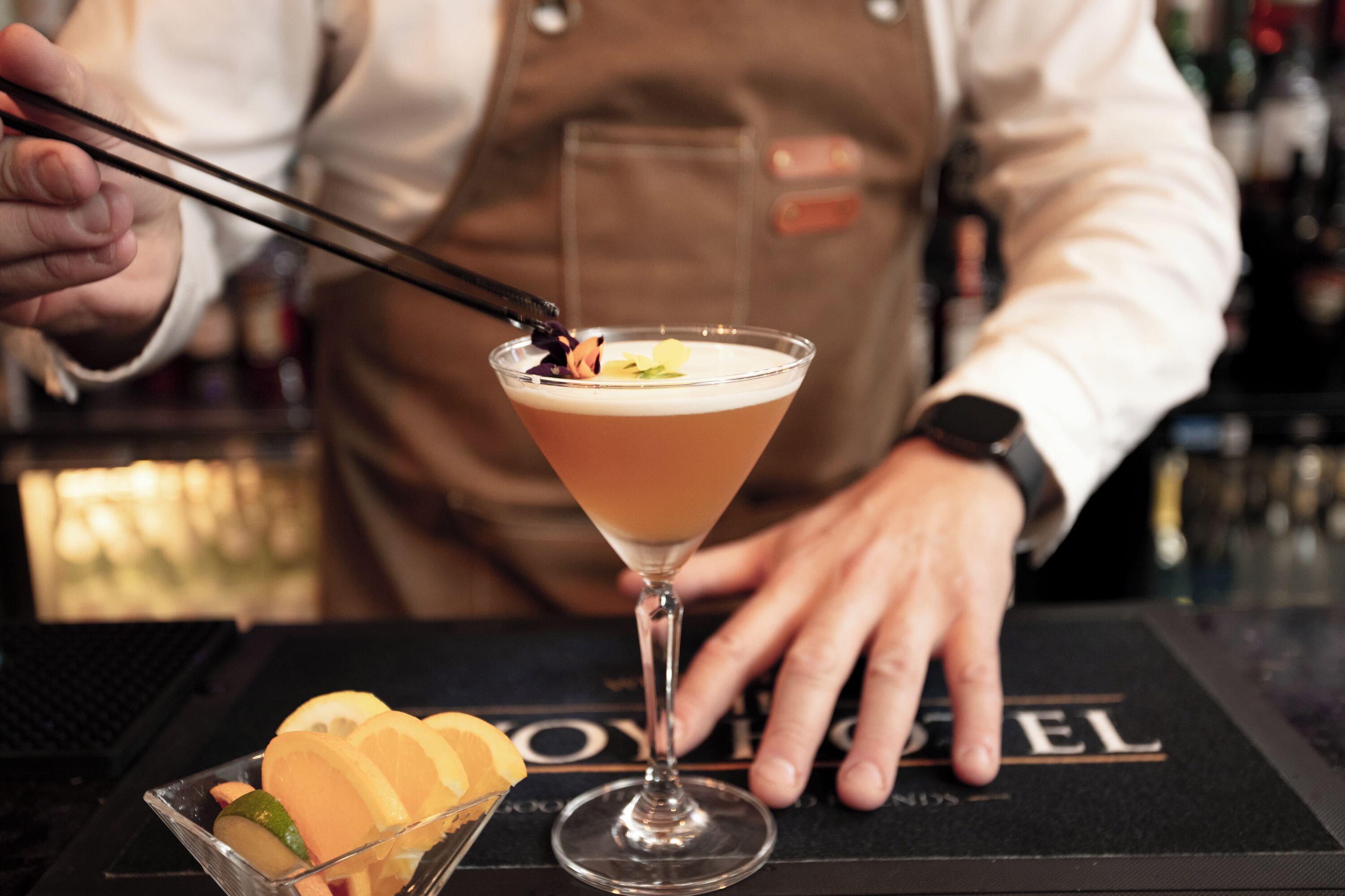 Um bartender preparando um coquetel com uma taça de martini sobre um tapete de bar com a inscrição "ROYAL".