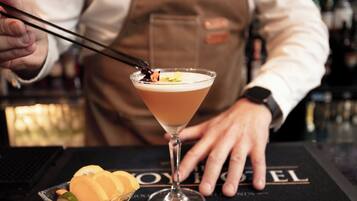 Um bartender preparando um coquetel com uma taça de martini sobre um tapete de bar com a inscrição "ROYAL".
