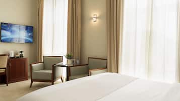 A hotel room with a large bed, two armchairs, a small table, a TV, and curtains.