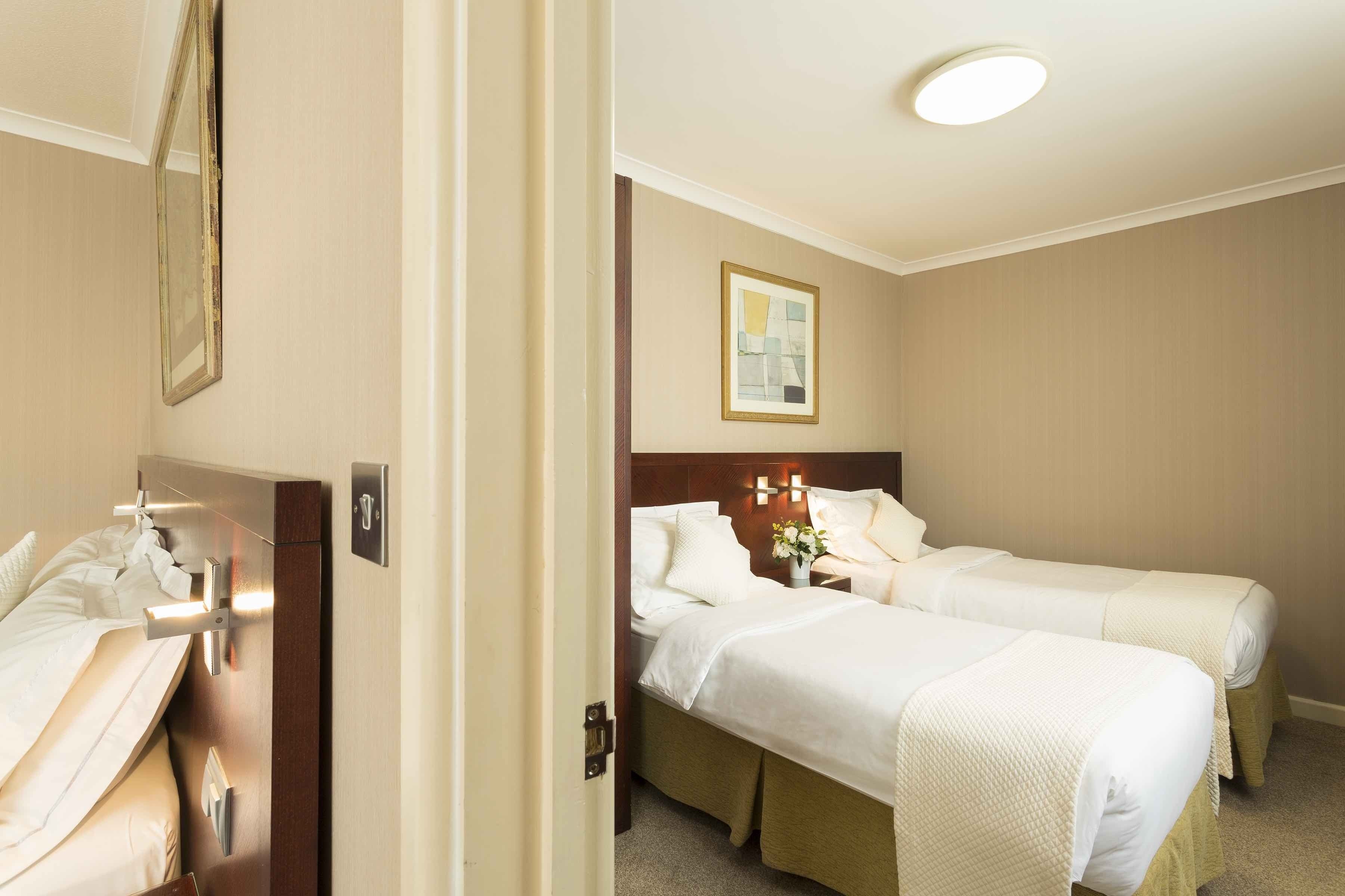 Ein Hotelzimmer mit zwei Betten, einem Holzkopfteil, einem Nachttisch mit Lampe sowie einem gerahmten Bild an der Wand.